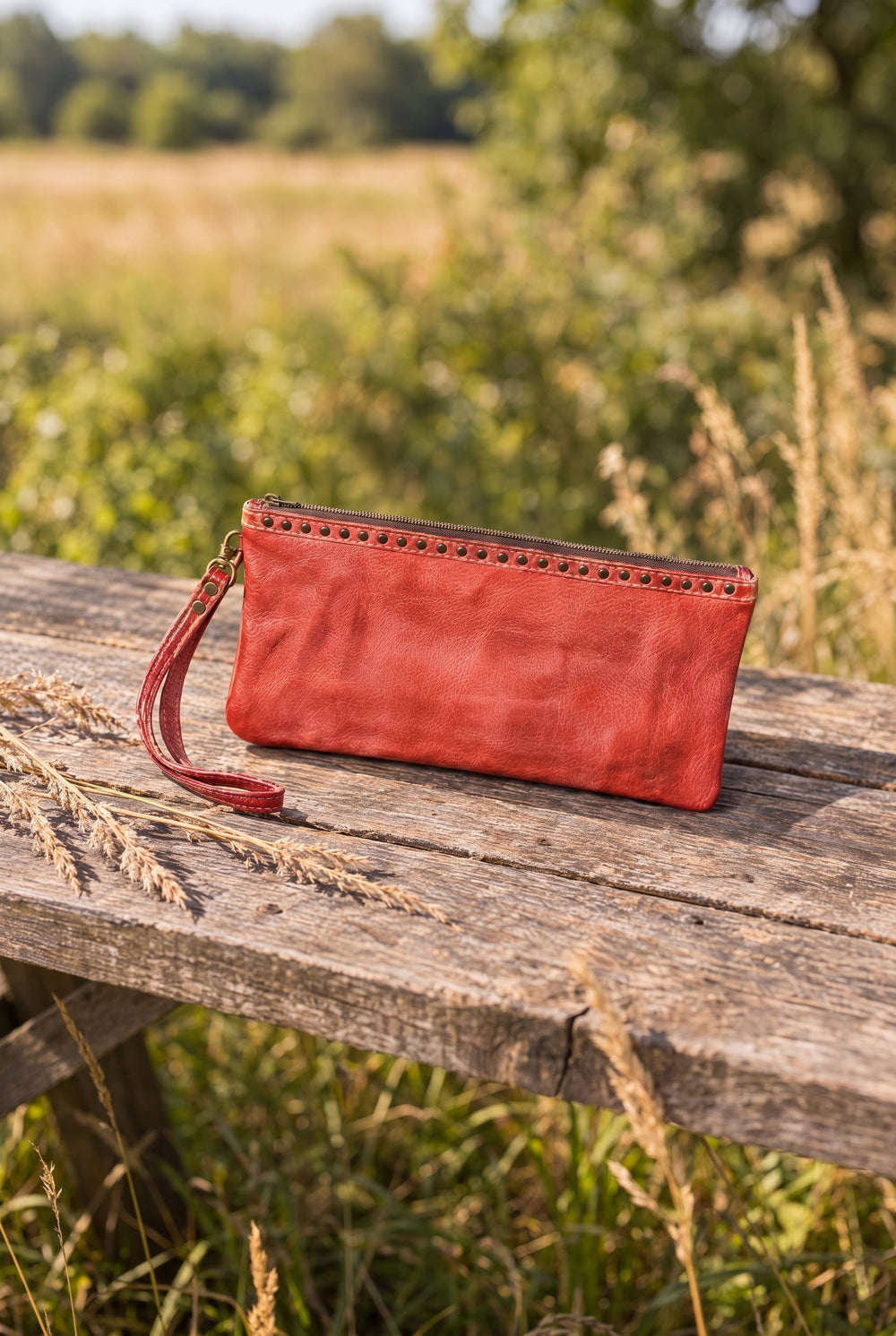 Red leather wristlet on a wood table outdoors