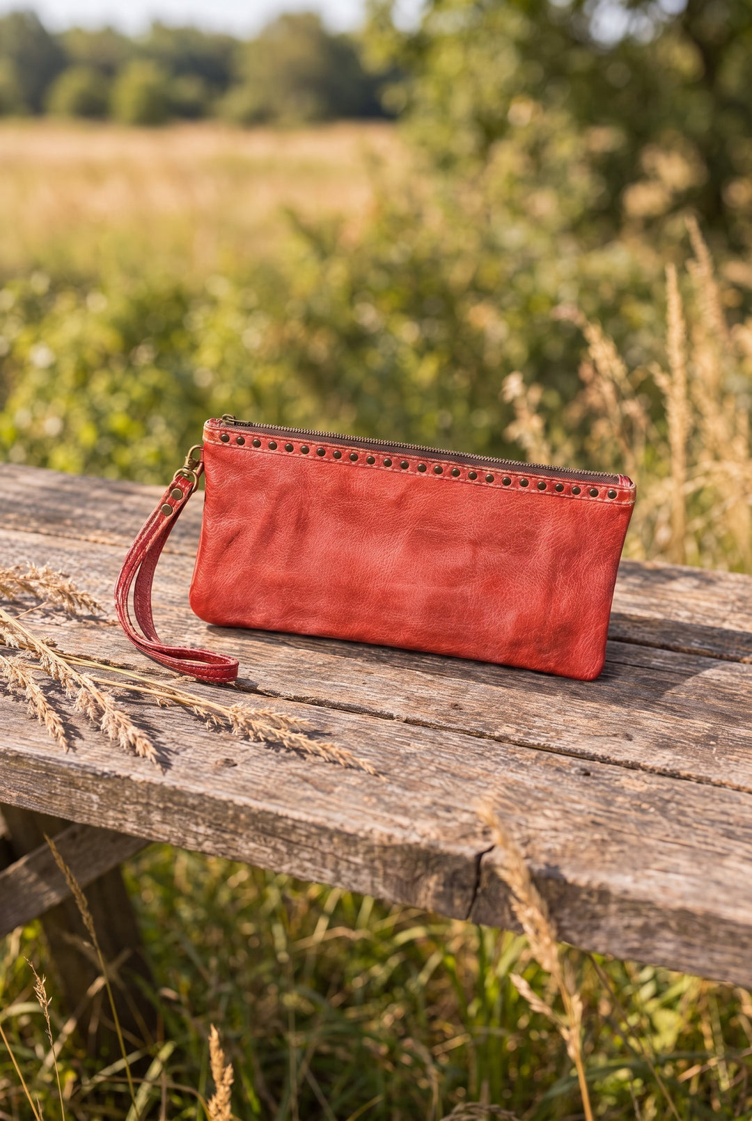 Red leather wristlet on a wood table outdoors