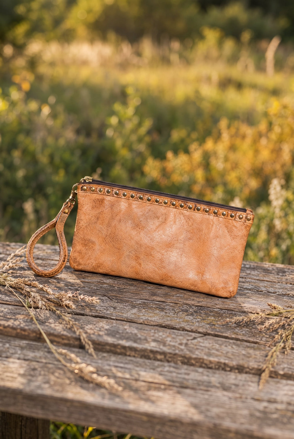 Tan leather wristlet on a wood table outdoors
