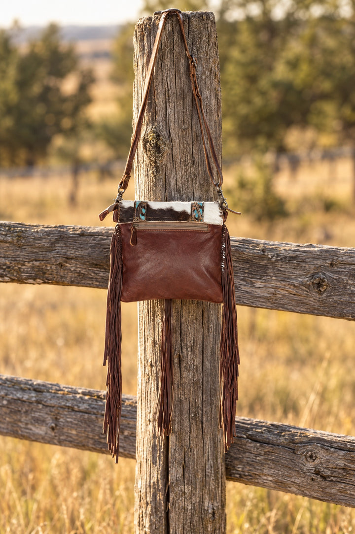 Dreamcatcher cowhide fringe crossbody hanging on a ranch fence