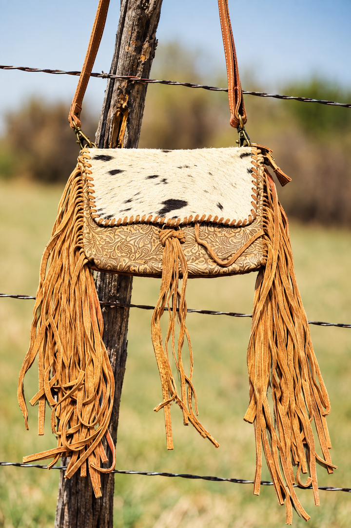 Hair on cowhide fringe crossbody on ranch fence