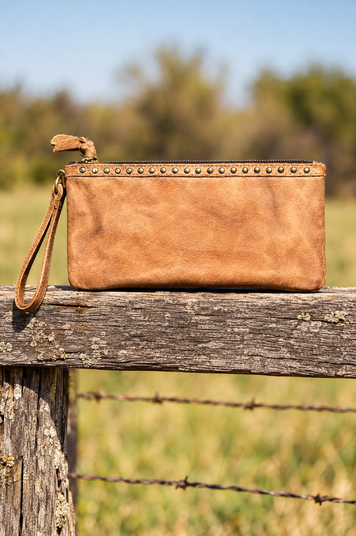 Tan leather wristlet pouch on ranch fence