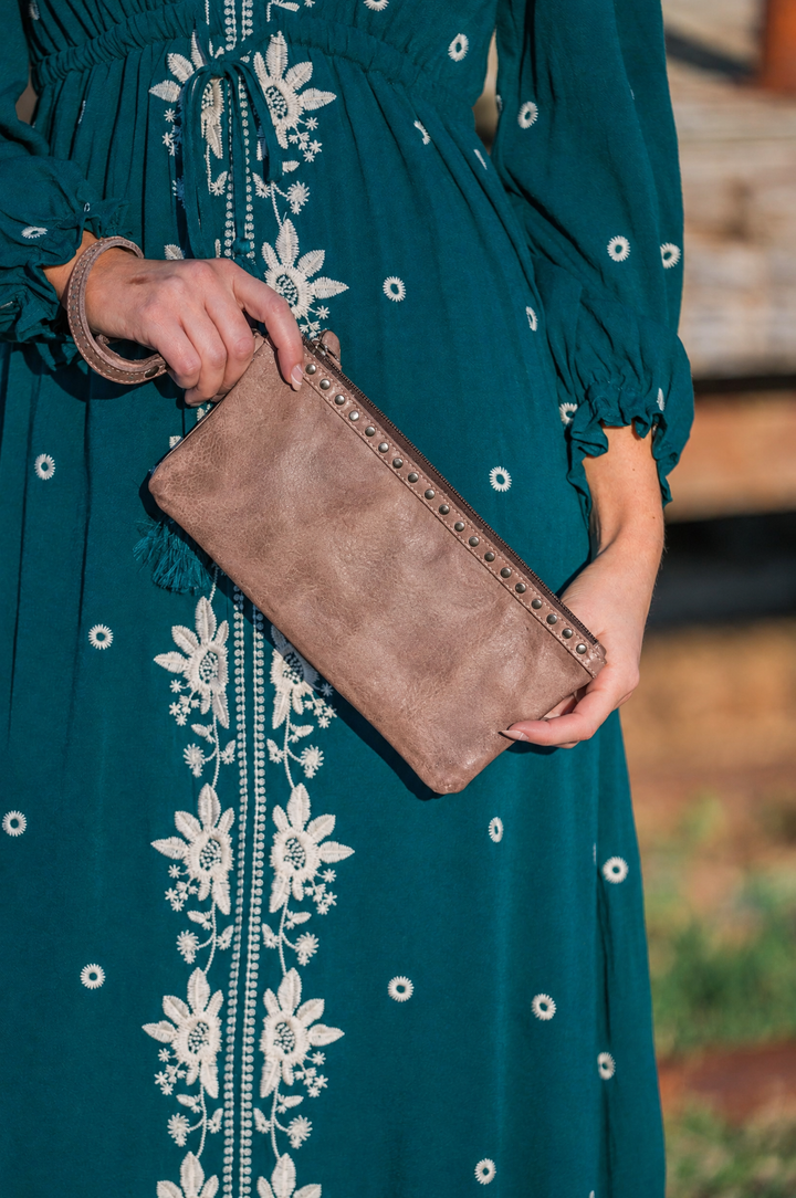 Brown leather studded wristlet held with a teal dress