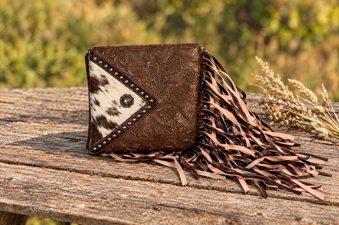 Embossed leather fringe wallet with cowhide triangle on a wood table