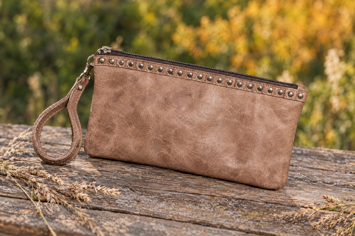 Brown leather wristlet on a wood table outdoors