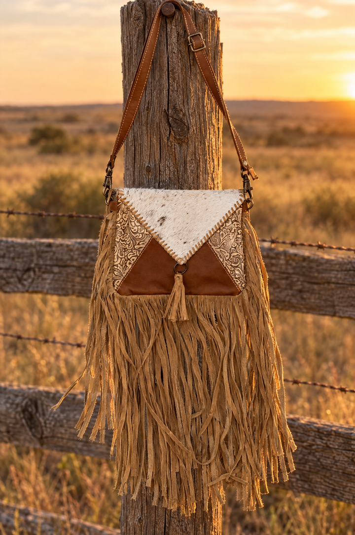 Tan suede fringe crossbody with cowhide triangle flap on a fence post