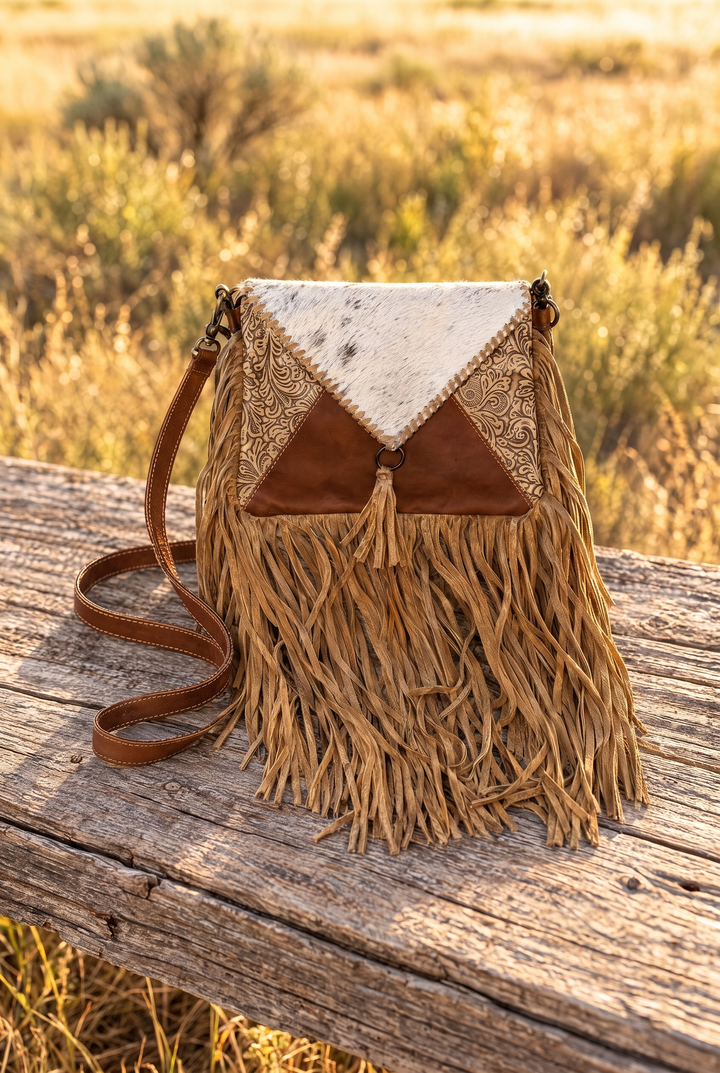 Golden Prairie cowhide and tooled leather fringe crossbody on a wood table